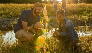 Photo of two students kneeling in a meadow to identify plants