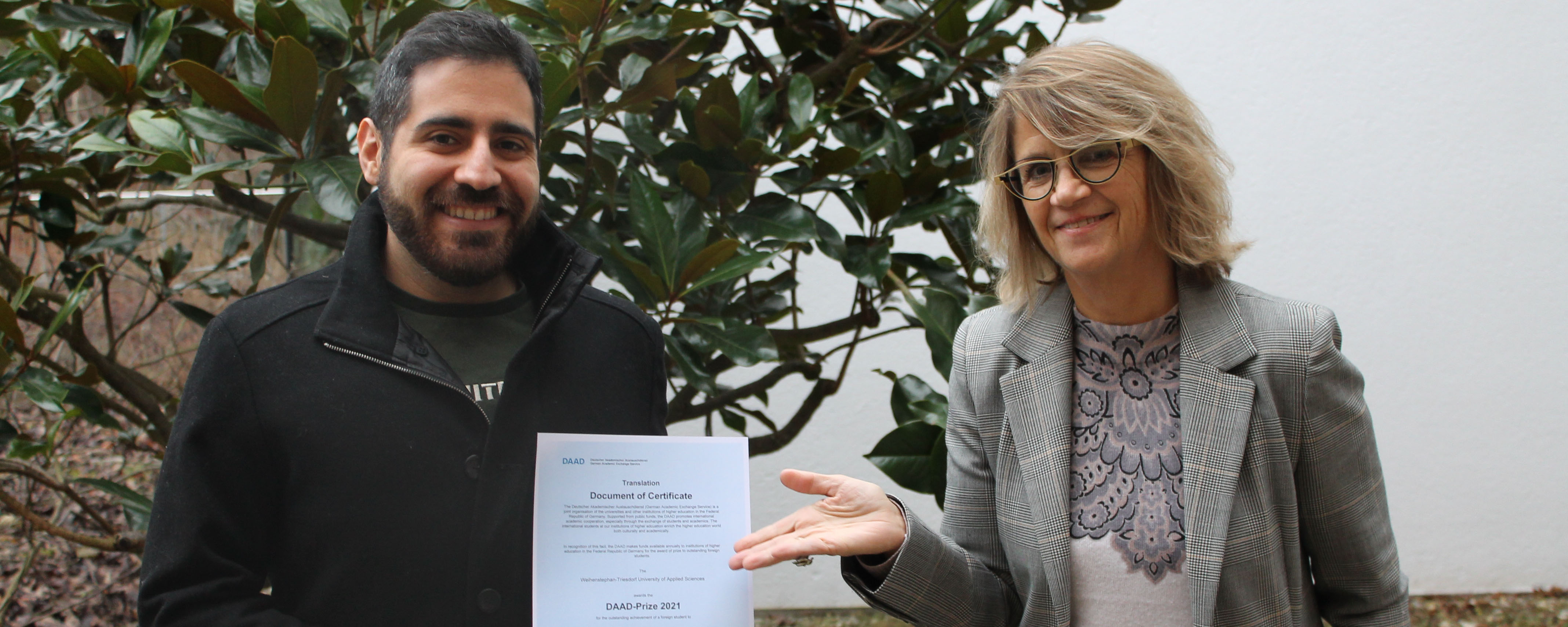 slide - Photo in the garden, background shrub. Paul Maksoud with certificate (left in picture), Prof. Ingrid Schegk (right in picture).