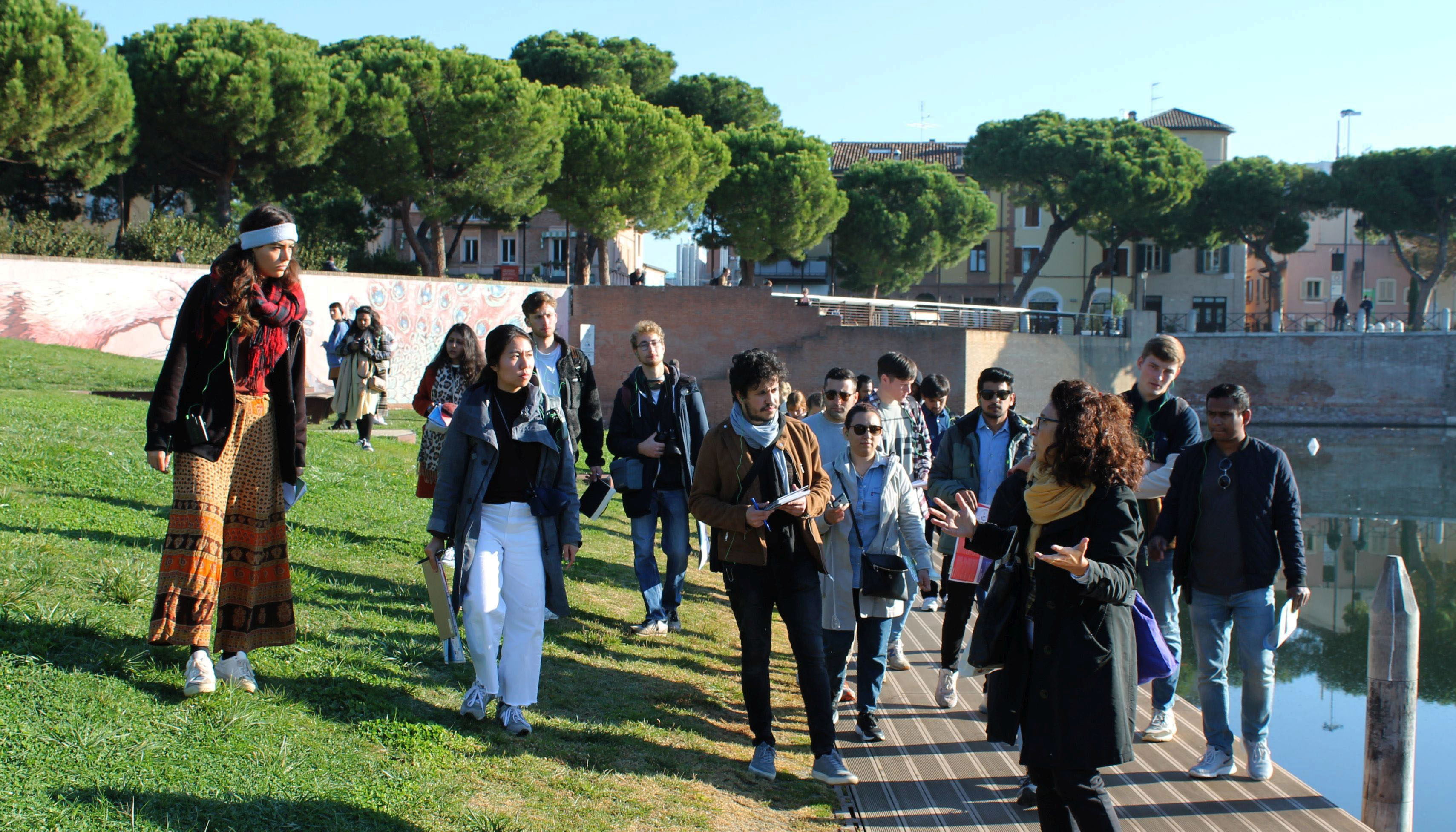 Photo river bank left, river right, guide and group of students, background river wall, trees and city