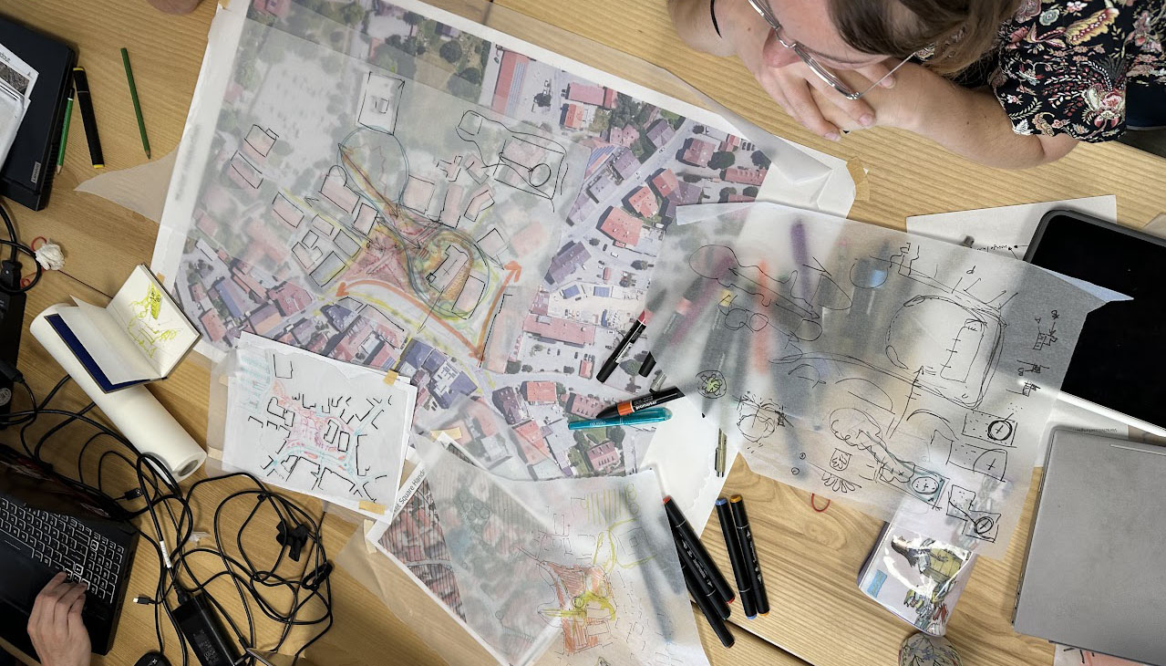 The image shows a top view of a table with plans, sketch paper, and pens on it.