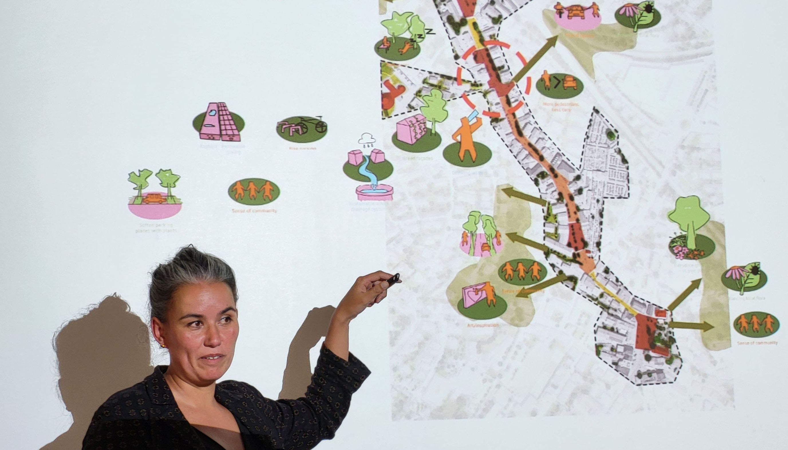 Photo detail showing a person standing on the left side of the image pointing to a map hanging on the wall on the right.