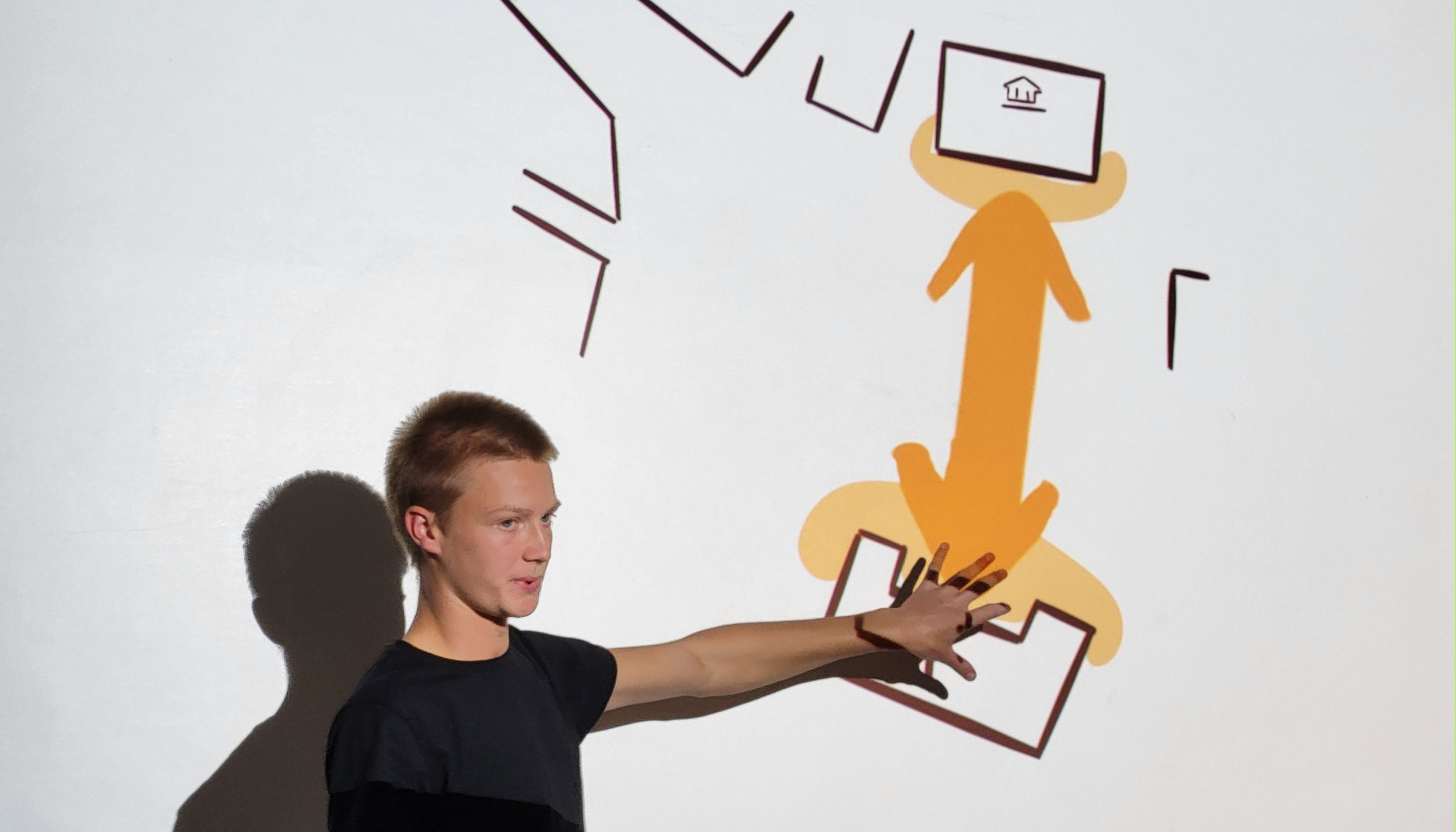 Photo detail showing a person standing on the left side of the image pointing to a map hanging on the wall on the right.