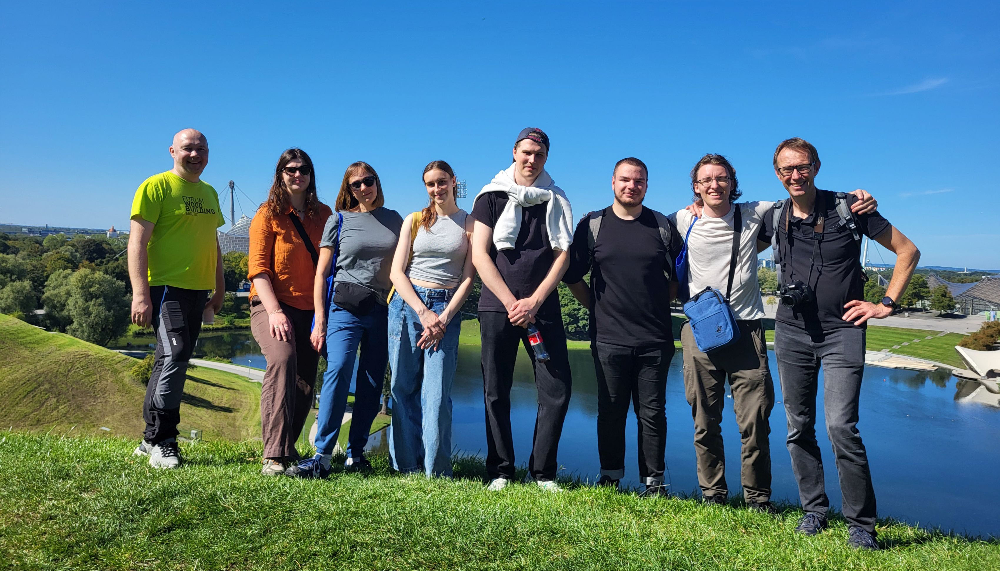 The image shows a section of a photograph of a group of people standing on a grassy hill and looking at the camera. A lake and buildings can be seen in the background.