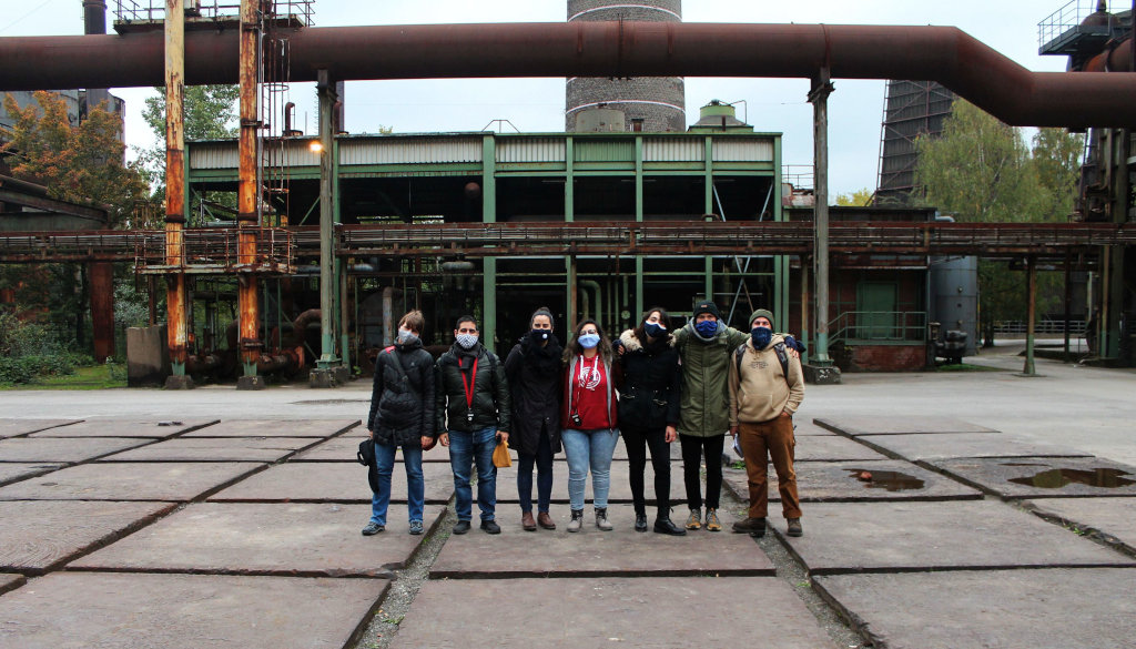 photo group of students with assistant on place with metal plates steel construction in the background