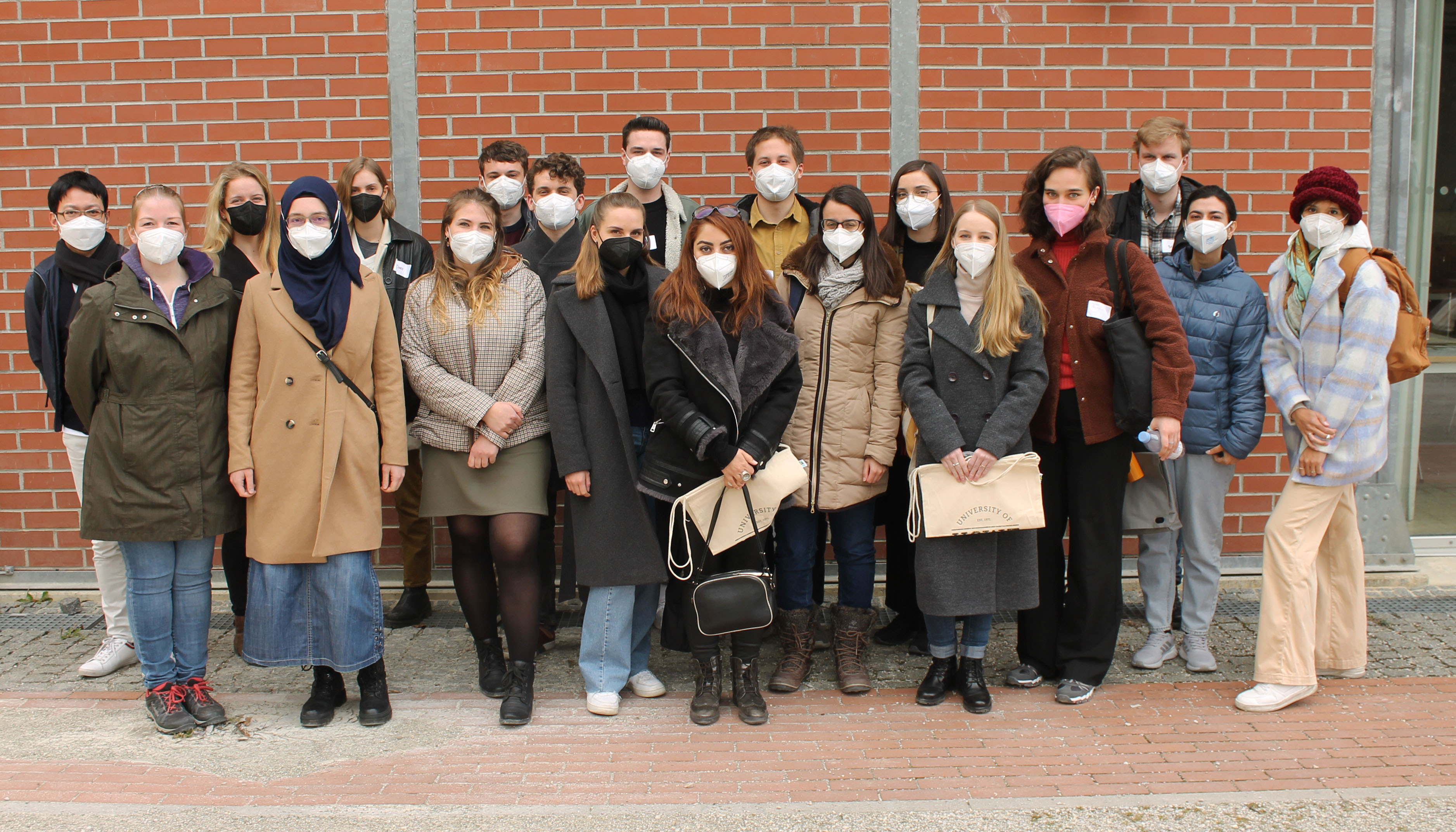 Photo group students with masks, on pavement, background house wall