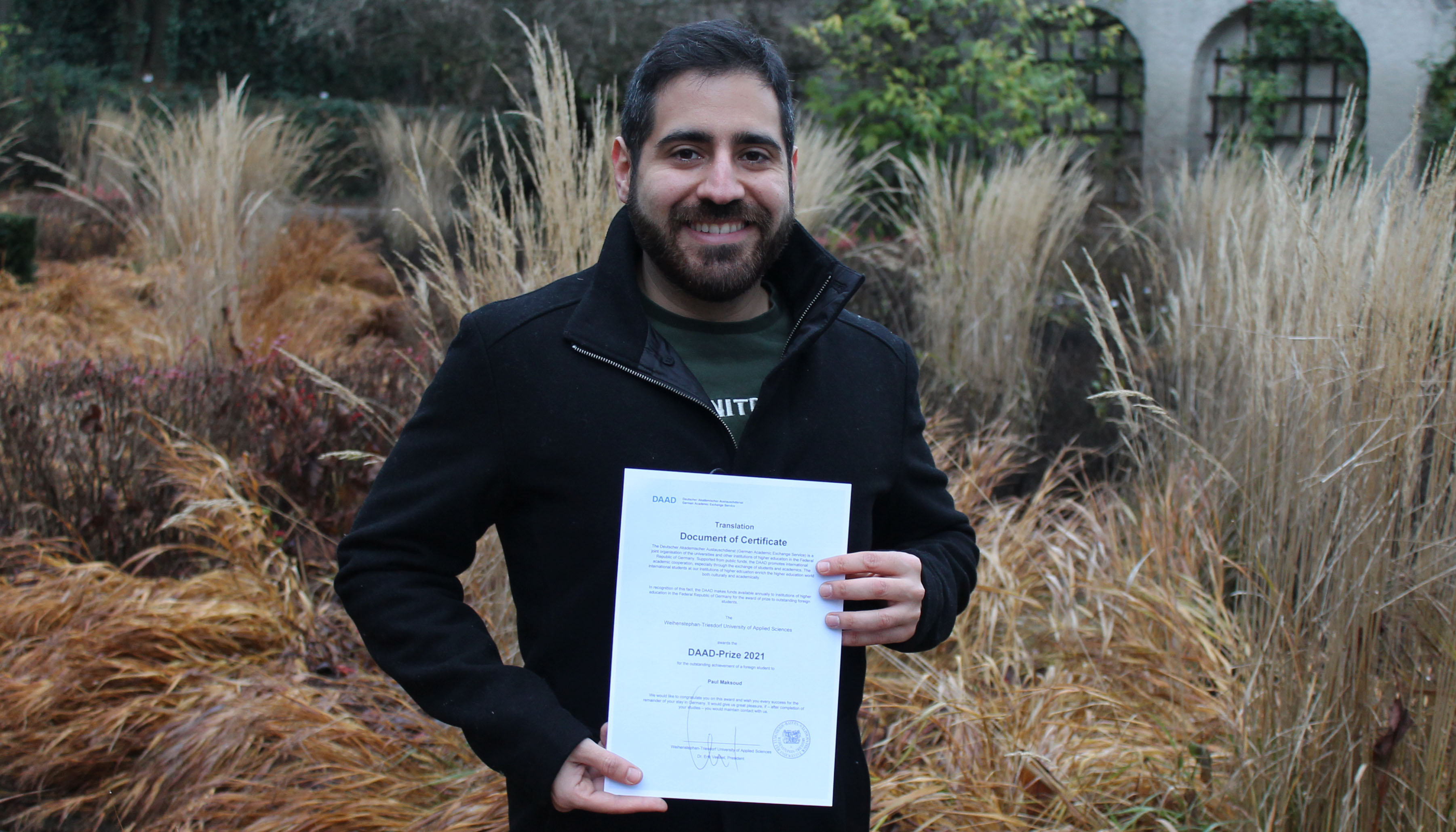 Photo in the garden, background shrub. Paul Maksoud with certificate.